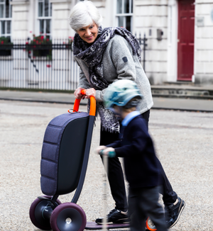 An older woman rides her Scooter for Life alongside her young grandson, who is riding a child’s scooter.