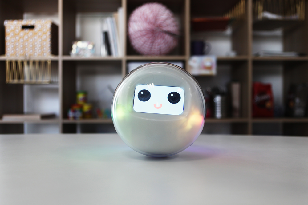 The smart toy Leka, a robotic sphere, rests on a table smiling through its digital interface.