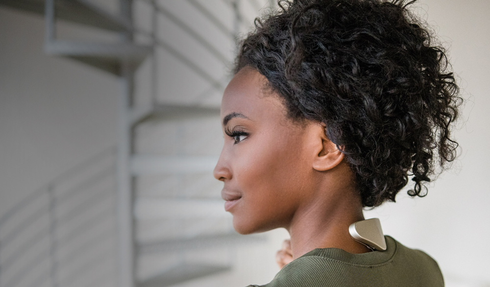 A woman wears the Thync Relax. The triangular device rests independently on the back of her neck.