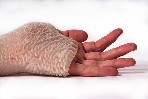 A close up of a human hand covered in the Carpal Skin prototype that is white with various ridges on the outside.